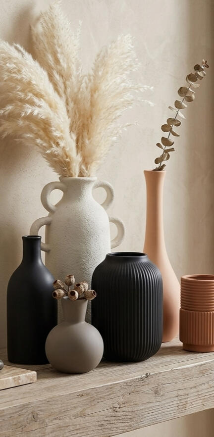 A collection of minimalist, organic-shaped vases in neutral tones like black, cream, and terracotta on a shelf.